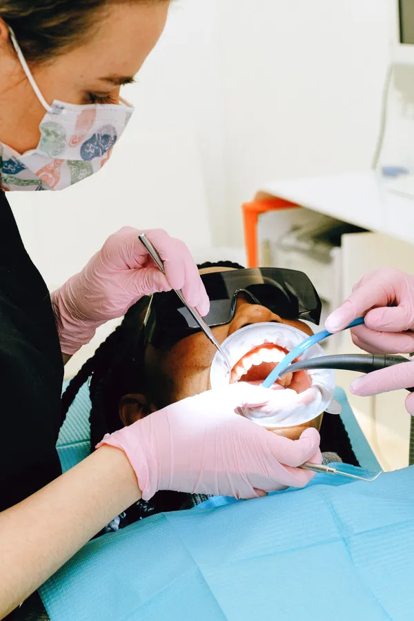 A hygienist cleaning a patient's teeth while the patient wears protective glasses